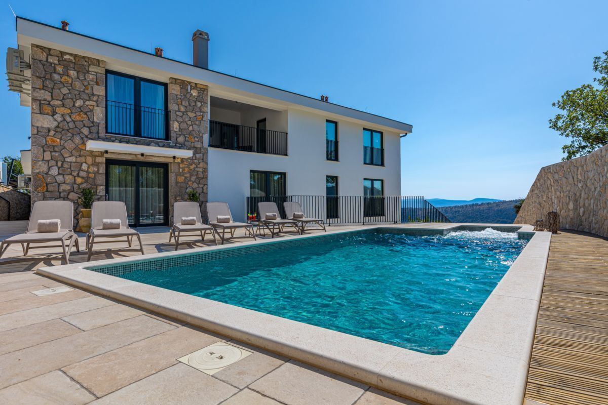A modern two-story house with a swimming pool, lounge chairs, and a view of the mountains.