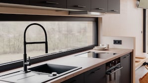 A modern kitchen with dark cabinetry, a stainless steel sink, and a window providing natural light. - Cabin Chalets House THREE (Geisa)