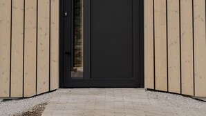 A modern building with a black door, wooden siding, and a small chimney. - Cabin Chalets House THREE (Geisa)