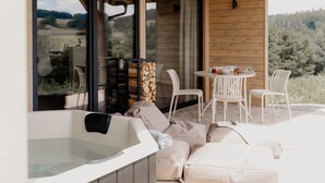 A cozy outdoor seating area with a hot tub, white chairs, and a table set for dining. - Cabin Chalets House THREE (Geisa)