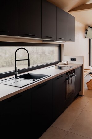 A modern kitchen with dark cabinetry, a stainless steel sink, and a window providing natural light. - Cabin Chalets House ONE (Geisa)