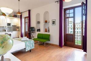 Una habitación con una cama, una silla verde, un globo terráqueo, un televisor y un balcón con vistas a edificios.