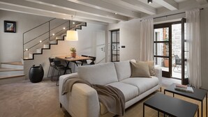 Un salon moderne comprenant un canapé, une table basse, un coin repas avec une table et des chaises, un escalier et une grande fenêtre avec des rideaux.