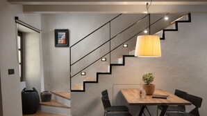 Un intérieur moderne avec un escalier, une table à manger, des chaises, un luminaire suspendu et une plante en pot.