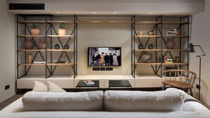 Un salon comprenant un canapé, une table basse, un téléviseur fixé au mur et deux étagères décoratives.