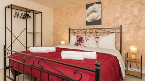 A neatly made bed with a red bedspread, a metal frame, and a wall-mounted coat rack with hangers. - Apartment 'Catania Del Mio Cuore' – Central, Sleeps 6, Family-Friendly (Catania)