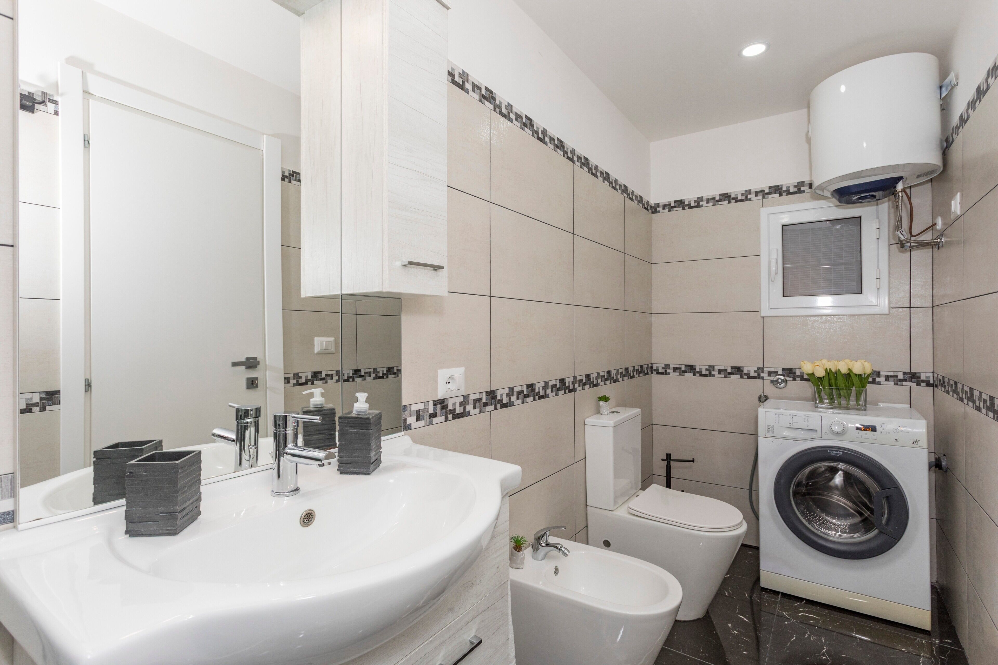 Et moderne badeværelse med vask, spejl, toilet, bidet og vaskemaskine.