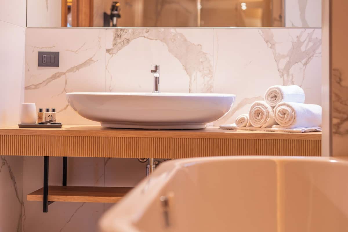 A modern bathroom with a large oval sink, wooden countertop, marble walls, and a visible shower area.