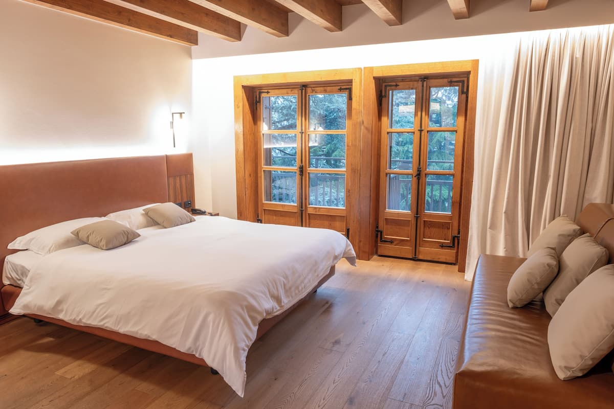 A bedroom with a large bed, wooden floor, and a window with curtains.