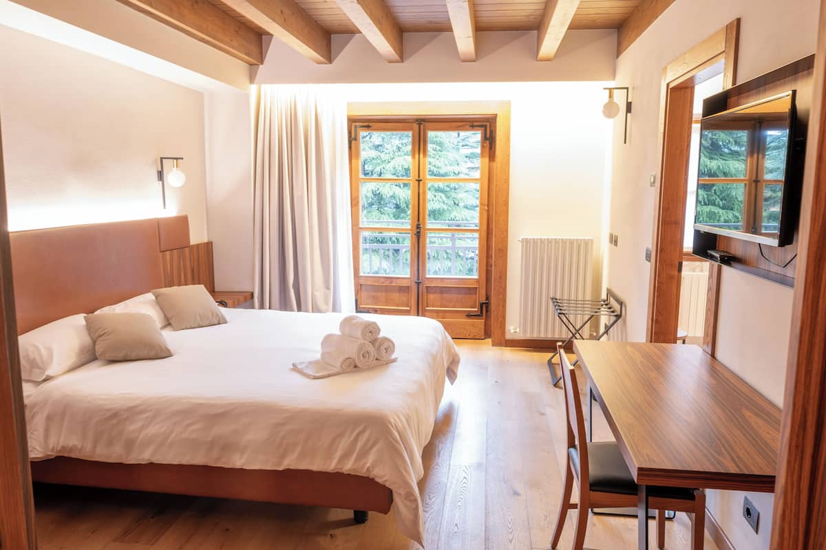 A bedroom with a wooden bed, a TV, and a window with curtains.