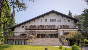 A large, two-story building with a balcony on the upper floor, stone steps leading to the entrance, and a well-maintained lawn in front. - Rosa delle Alpi (Esino Lario)
