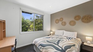 Ein Schlafzimmer mit Bett, Schreibtisch, Stuhl, Fenster mit Blick auf Bäume und Wanddekoration.