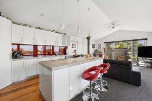 A modern kitchen with white cabinets, a central island, and red bar stools. - Point View Beach House (Lorne)