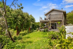 A two-story house with a balcony, surrounded by lush greenery and trees. - Point View Beach House (Lorne)