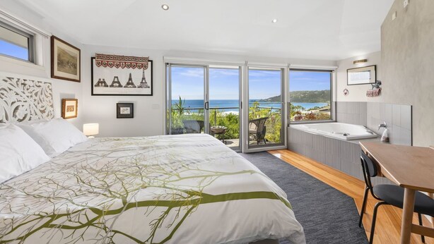 Ein modernes Schlafzimmer mit einem großen Bett, Meerblick, einem Balkon und einem Badezimmer mit einer Badewanne.
