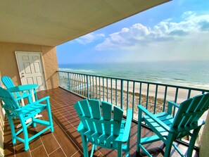 Ein Balkon mit türkisfarbenen Adirondack-Stühlen, einer Tür und Blick auf Strand und Meer.