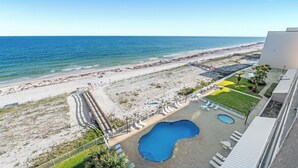 A beach view from a hotel balcony with a swimming pool and outdoor seating. - Gorgeous Beachfront;  Walk to restaurants! (Gulf Shores)