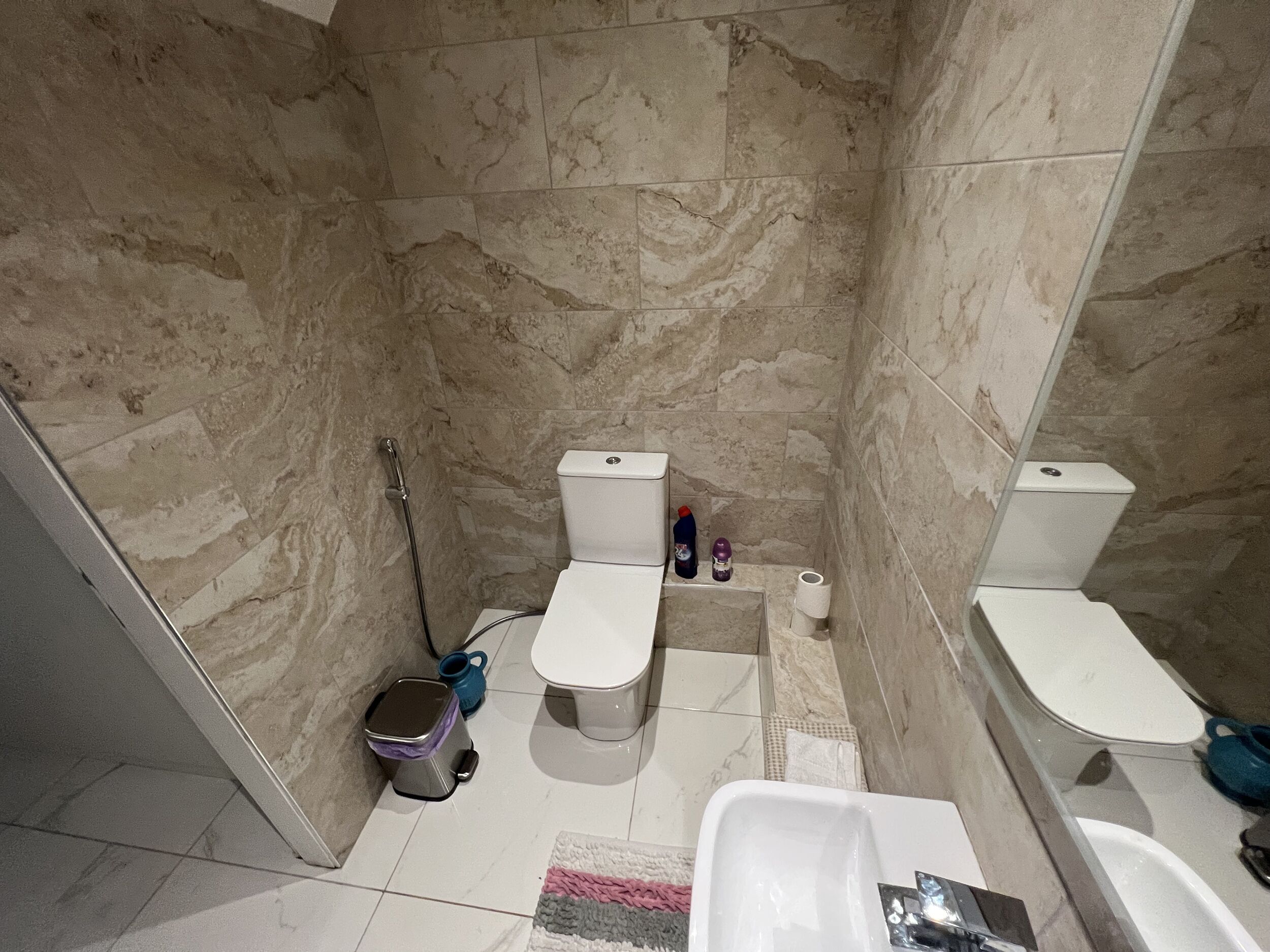 A bathroom with two toilets, a shower, a sink, and a trash bin.