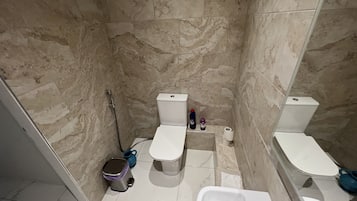 A bathroom with two toilets, a shower, a sink, and a trash bin.