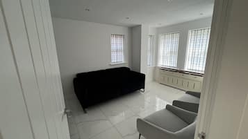 A spacious living room with a black sofa, a grey armchair, and a radiator under large windows.