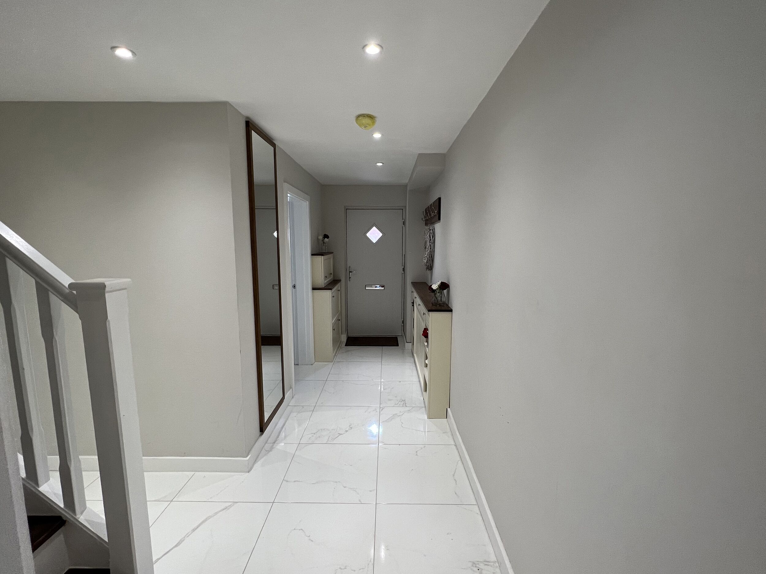 A hallway with a marble floor, a staircase on the left, and a door at the end.