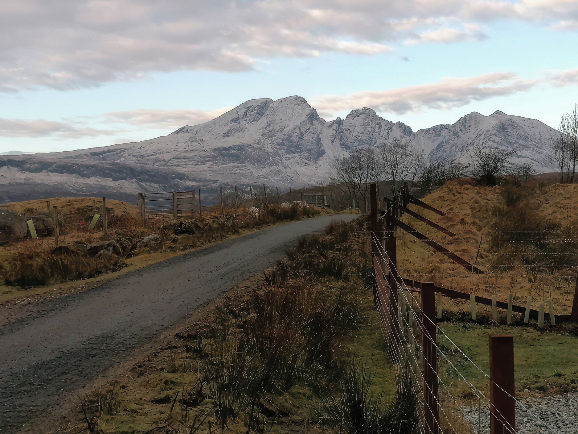 A rural road leading to a mountain range with a fence on one side.
