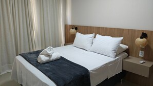 Ein ordentlich bezogenes Bett mit weißen Leinen und einer dunkelblauen Decke, ein Holzkopfbrett, zwei Nachttischlampen und ein gefaltetes Handtuch auf dem Bett.