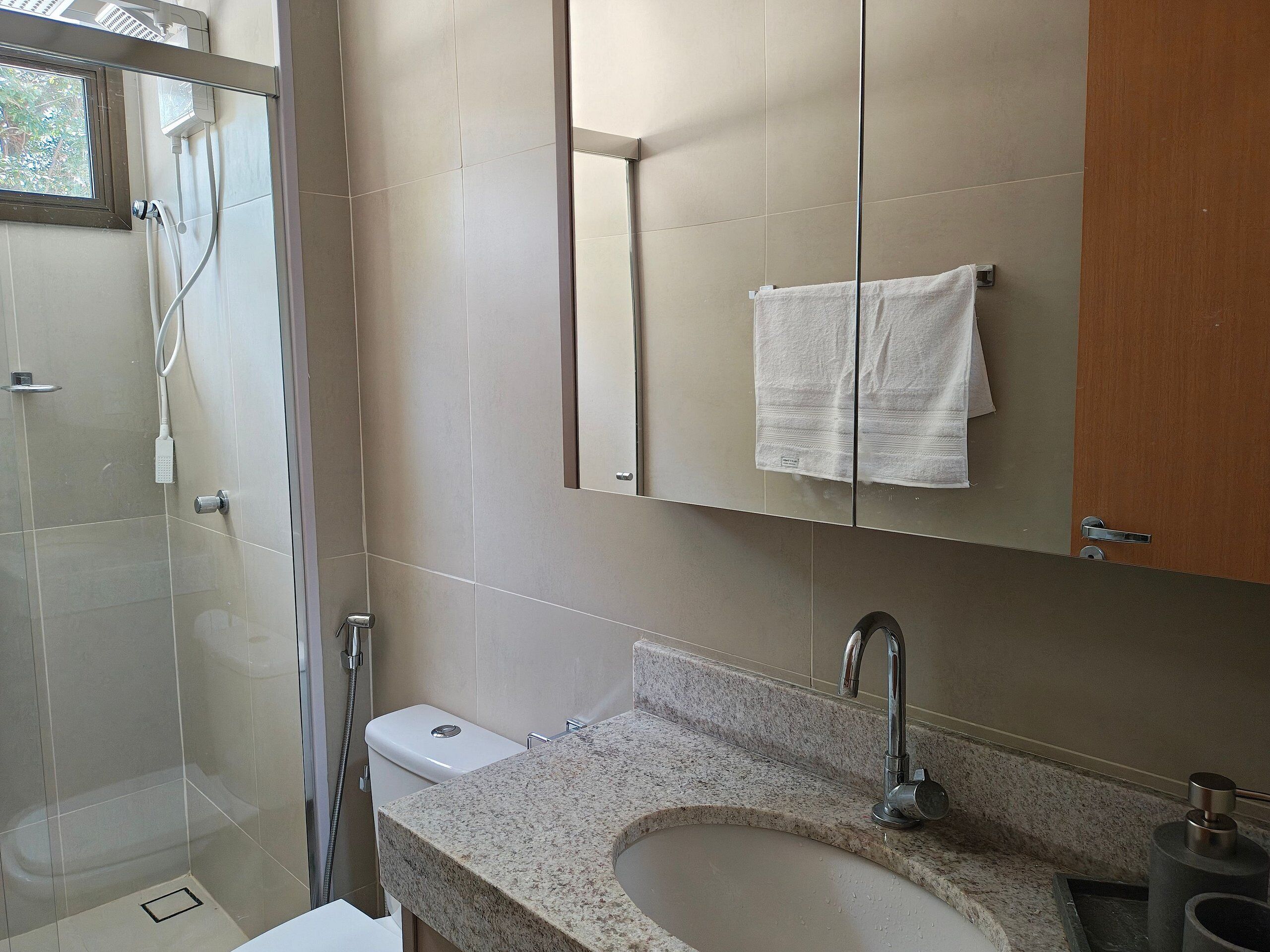 Een moderne badkamer met douche, toilet, wastafel en een spiegel boven de wastafel.