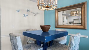 A dining area with a blue table, patterned chairs, a wooden bowl, and a chandelier. - Ground level Gulf front condo, w/ pool, grill & gazebo ~ Sleeps 4 (Orange Beach)