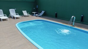 En swimmingpool med blå kant, omgivet af hvide liggestole og et lille bord.