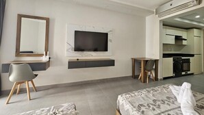 Una habitación de hotel moderna con cama, escritorio, silla, televisor y kitchenette.