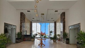 Un hall d’entrée spacieux, avec une table centrale, des plantes en pot et une vue sur les bâtiments à travers de grandes fenêtres.
