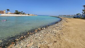 Una playa con agua cristalina, un litoral rocoso y un muelle que se adentra en el mar.
