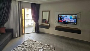 Una habitación de hotel moderna con una cama grande, un televisor de pantalla plana montado en la pared, un sofá y un ventanal corredero que da a un espacio al aire libre.