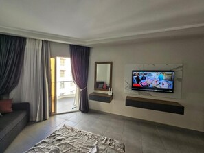 A modern hotel room with a large bed, a flat-screen TV mounted on the wall, a sofa, and a sliding glass door leading to an outdoor area. - Scandic Resort C310 (Hurghada)