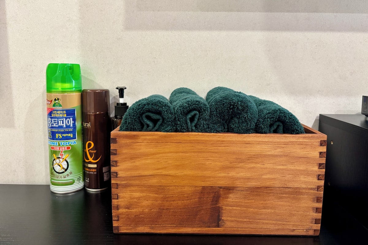 A wooden box containing green towels, a green bottle of insect repellent, and a brown bottle of lotion on a dark surface.
