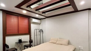 A bedroom with a bed, a small table with chairs, a window with blinds, and an air conditioning unit. - Daegu Chilgok Money Stay 2nd Branch (Chilgok)