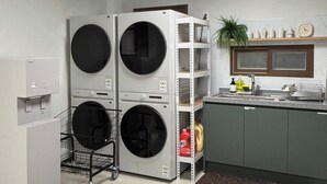 A laundry room with two stacked washing machines, a metal cart with a basket, a sink, and a shelf with various items. - Daegu Chilgok Money Stay 2nd Branch (Chilgok)