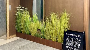 A reception area with a wooden reception desk, a check-in sign, and a large mirror reflecting the elevator. - Daegu Chilgok Money Stay 2nd Branch (Chilgok)