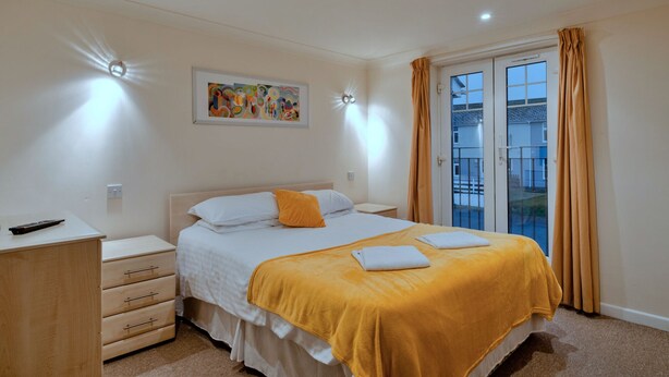 Une chambre à coucher avec un lit, une table de chevet, une commode, une fenêtre avec des rideaux et un tableau au mur.