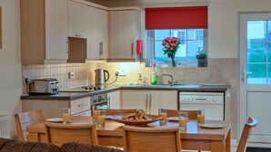 Une cuisine moderne avec des meubles en bois, une table à manger avec des chaises et une fenêtre avec un store rouge.