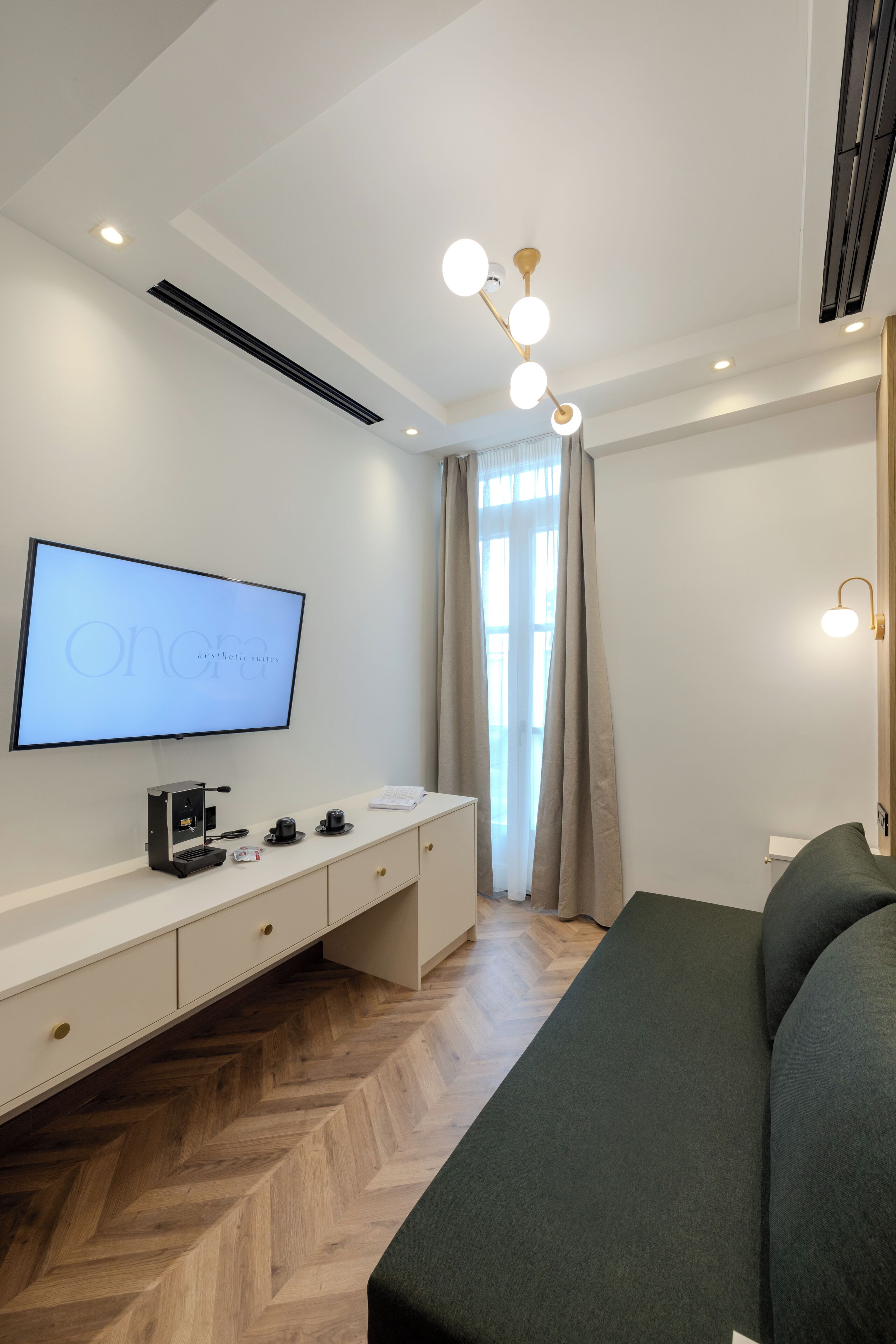 Une chambre d’hôtel moderne dotée d’une télévision à écran plat, d’une machine à café, d’un canapé et d’un parquet en bois à motifs en chevrons.