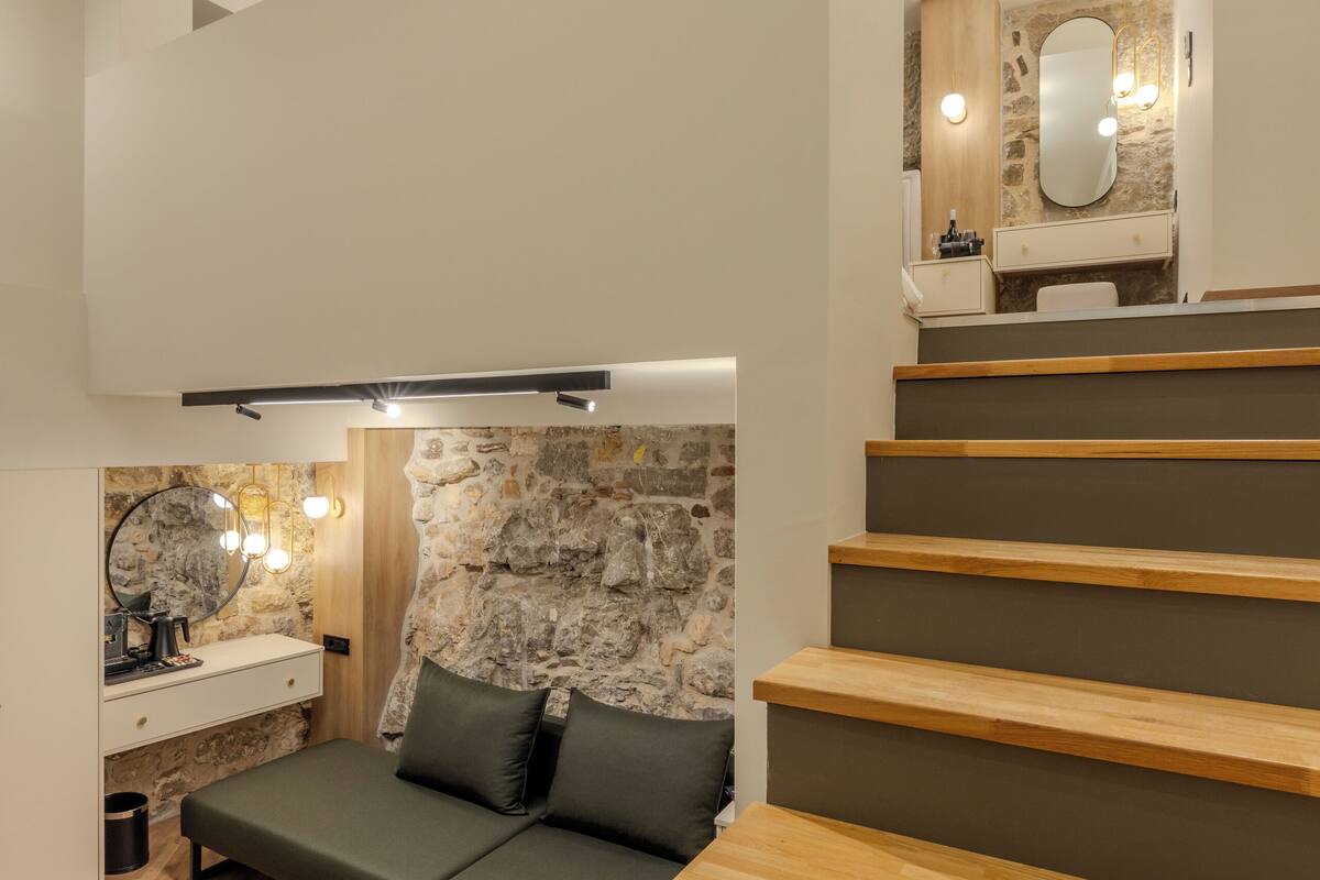 A modern bedroom with a loft bed, a stone accent wall, and a bathroom with a mirror and sink.