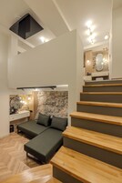 Un dormitorio moderno con cama alta, pared de acento de piedra y baño con espejo y lavamanos.