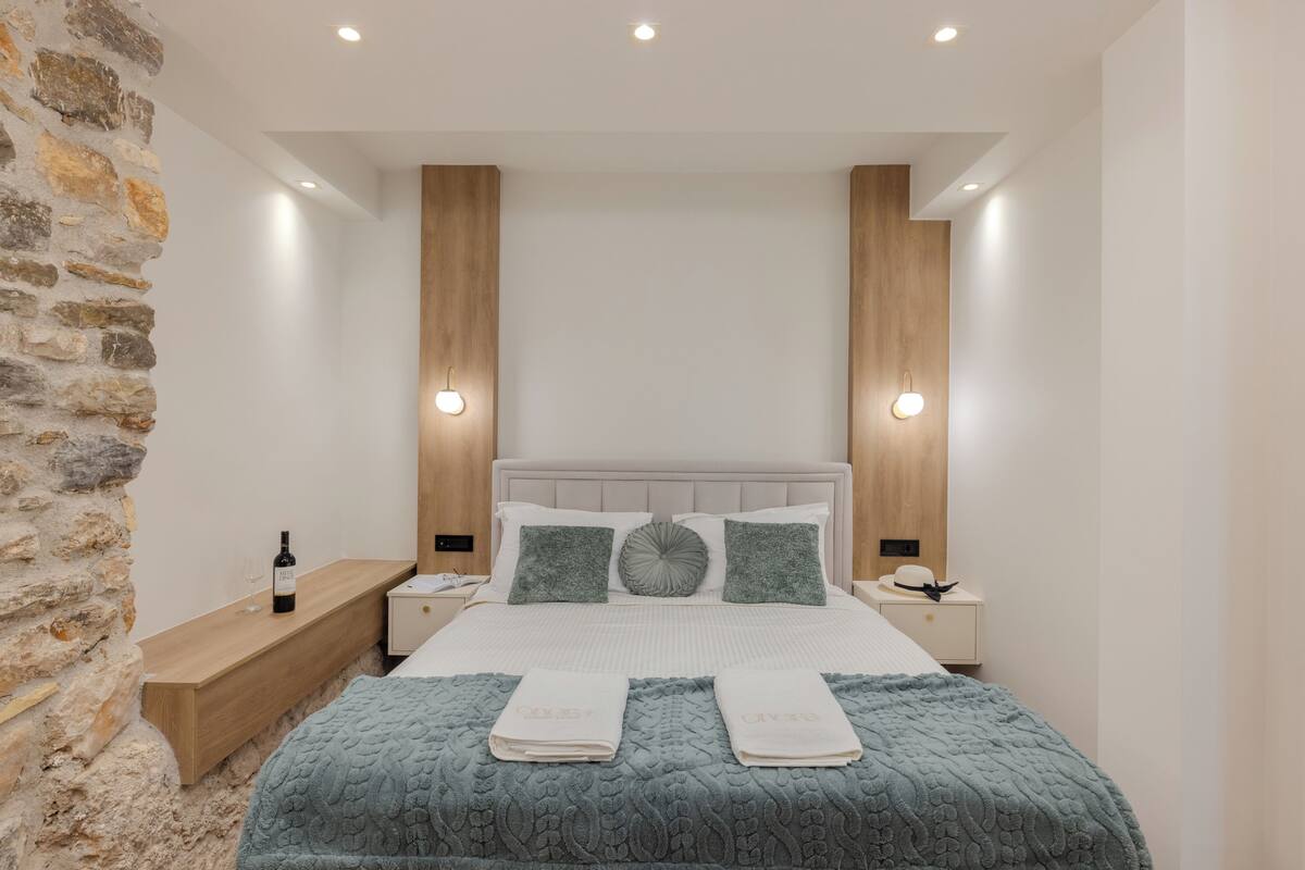 A modern bedroom with a stone accent wall, a wooden headboard, and a bed with two pillows and a blanket.