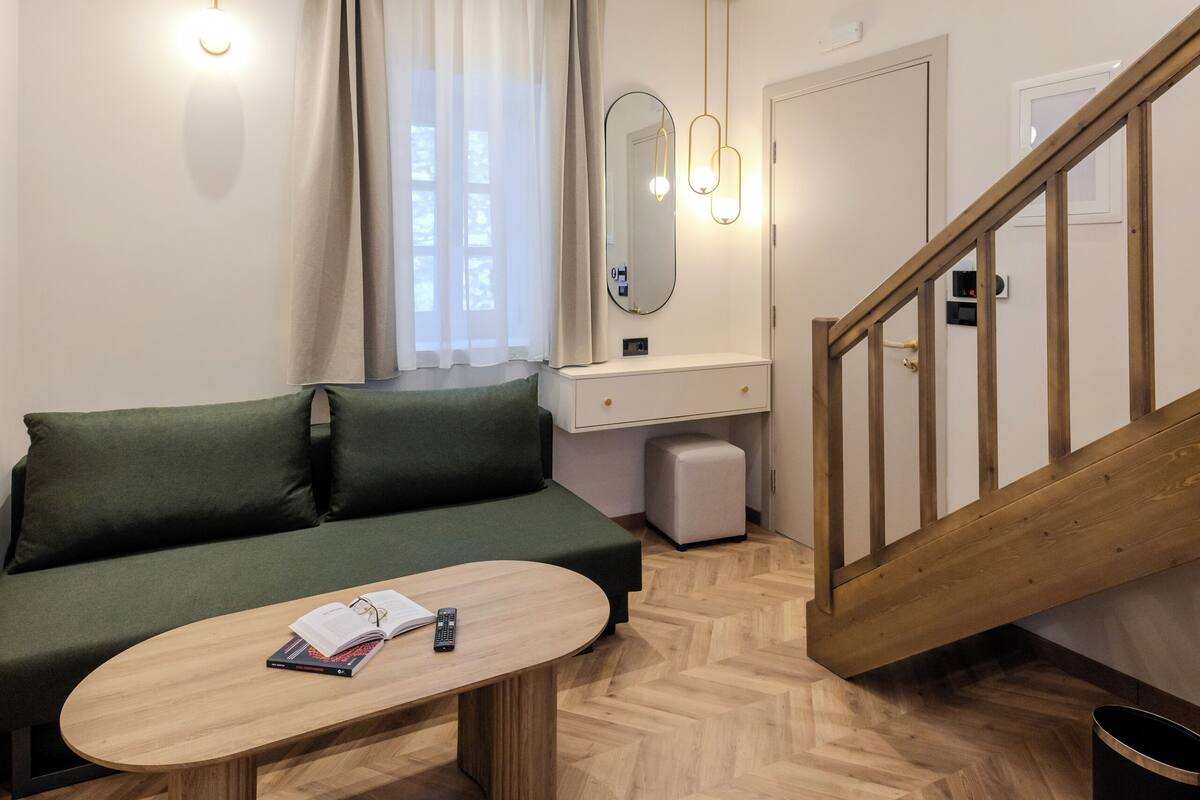 A modern living room with a wooden herringbone floor, a green sofa, a wooden coffee table, and a staircase with wooden railings.