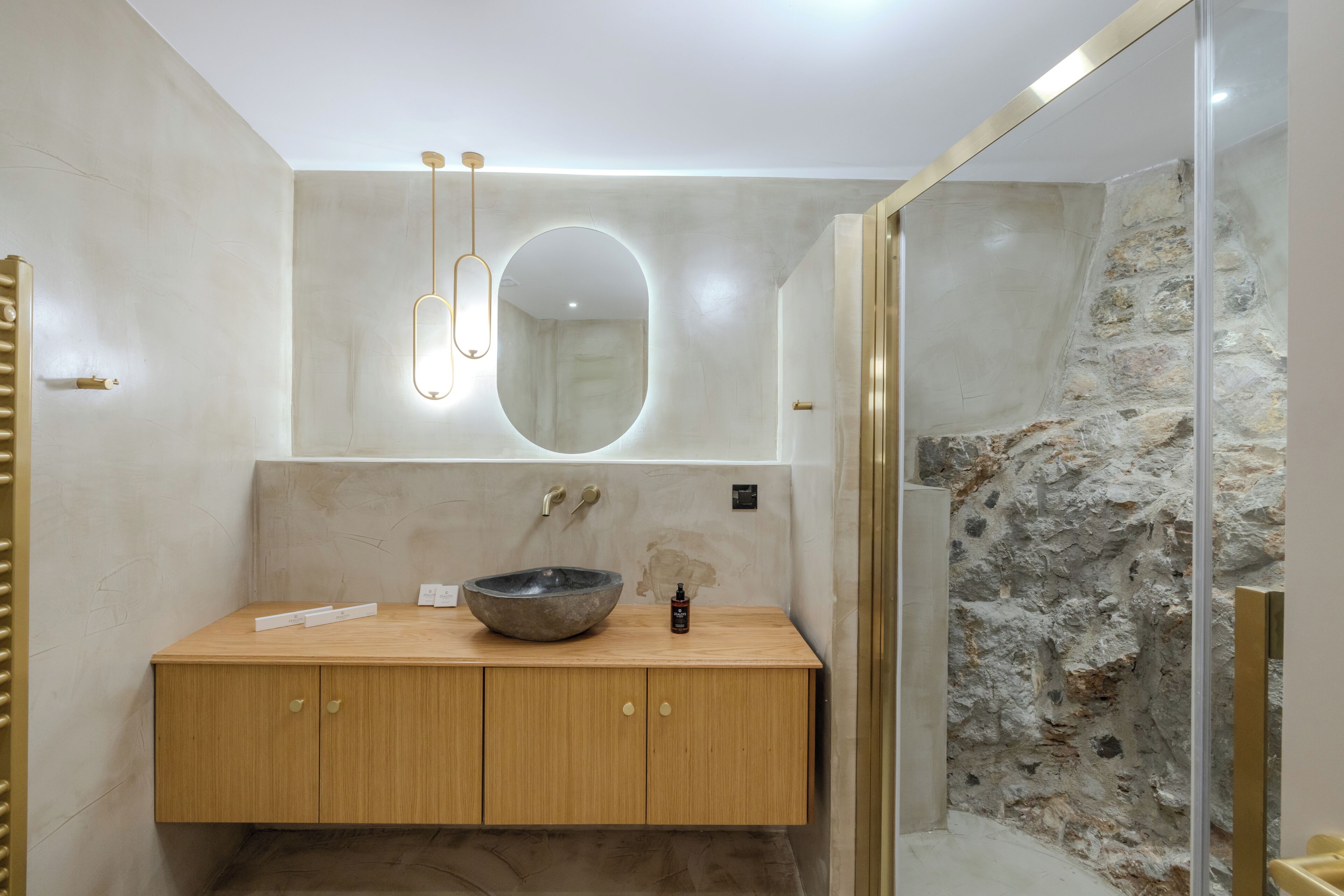 A modern bathroom with a wooden vanity, a large round mirror, and a stone accent wall.
