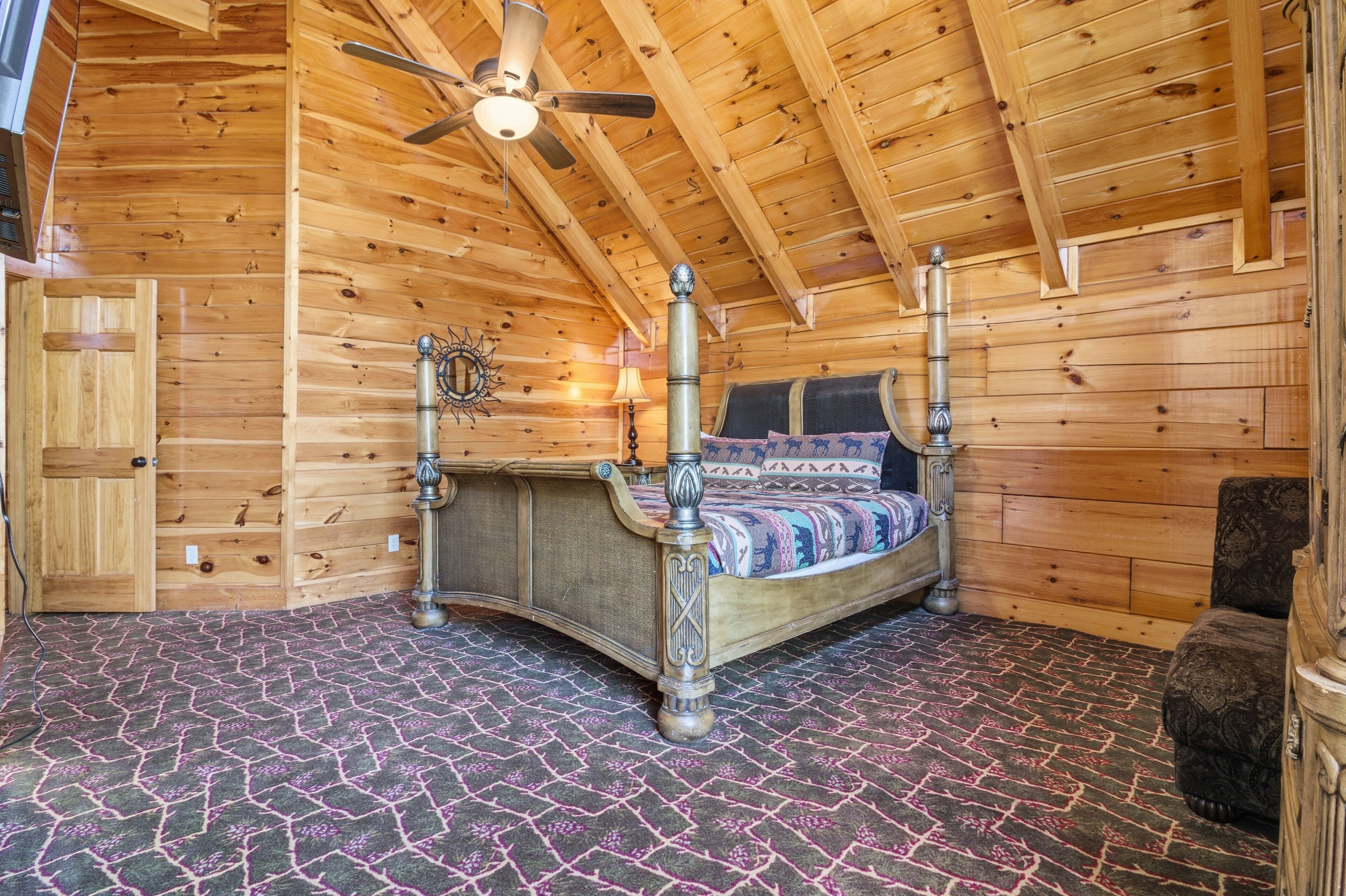Een slaapkamer in een houten blokhut met een bed, een plafondventilator en een kamerbreed tapijt met dessin.