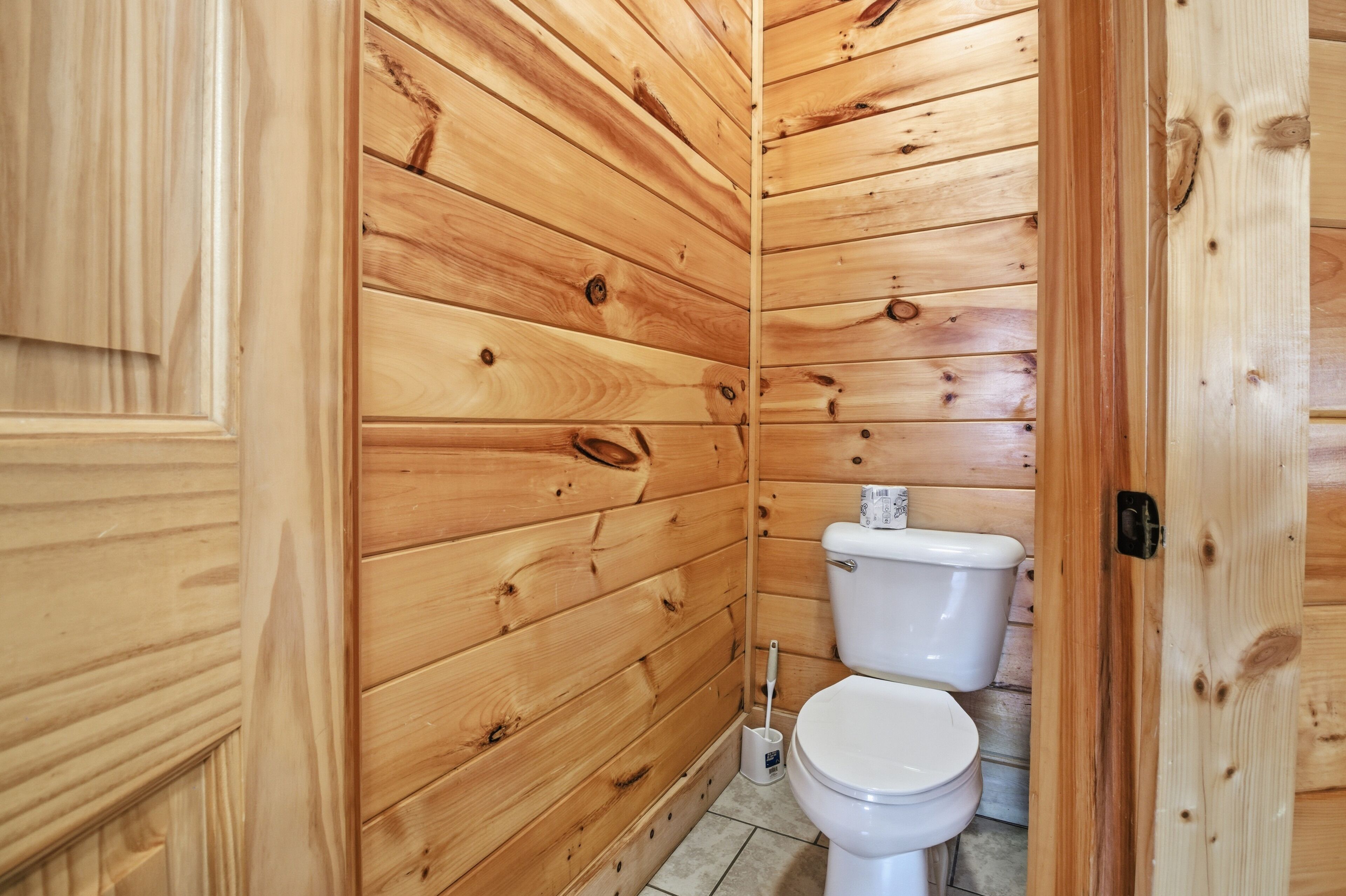 A wooden-paneled bathroom with a toilet and a broom.
