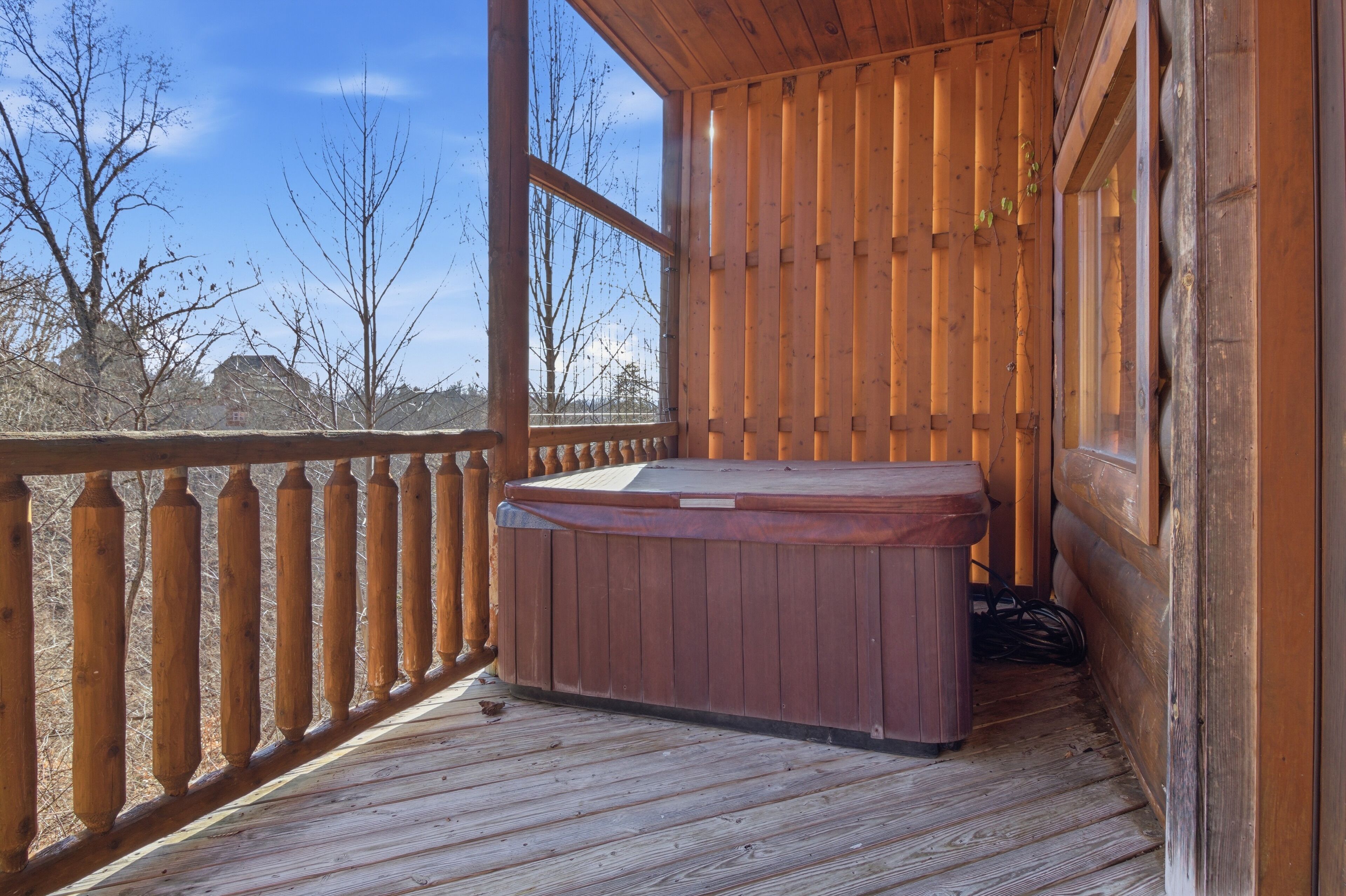 Una terraza de madera con un jacuzzi, barandillas de madera y vistas a árboles y edificios.